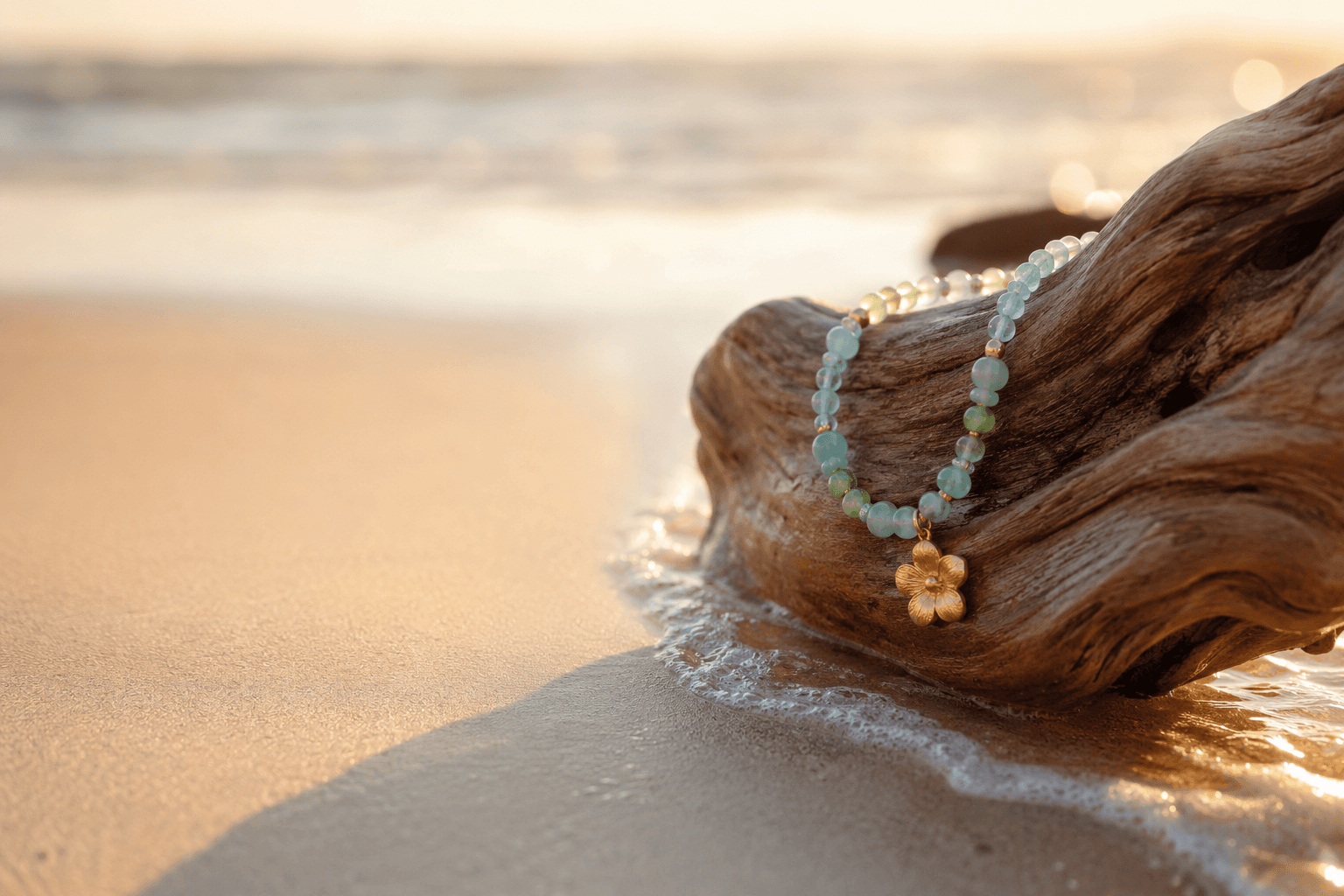 Collar de aguamarina y jade sobre un tronco de madera de deriva mientras el mar sube por la arena