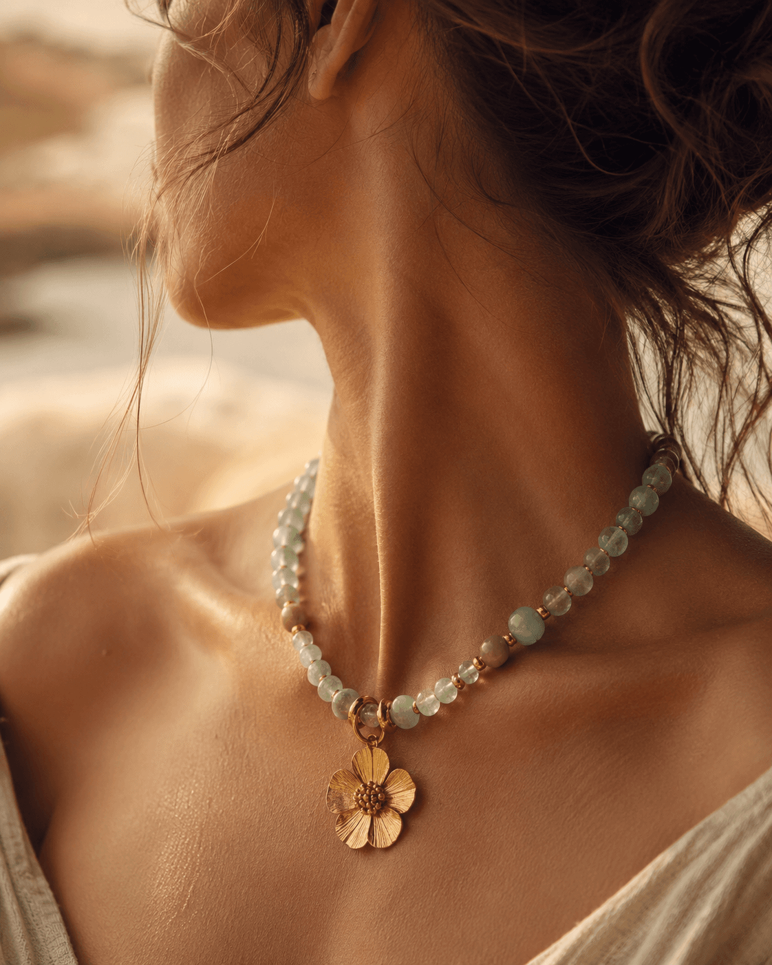 Primer plano del cuello de una mujer luciendo un collar de aguamarina y jade con dije de flor dorada