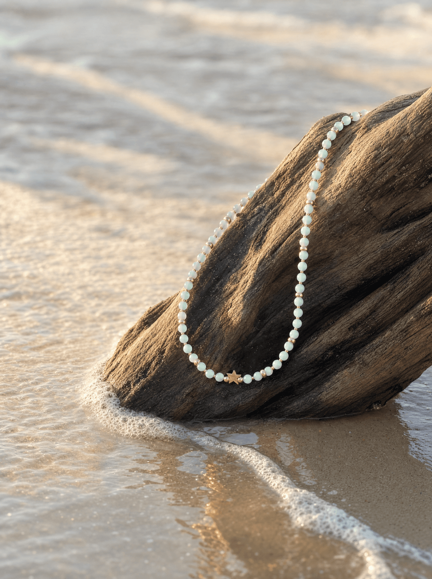 Collar de amazonita sobre madera de deriva a la orilla del mar al atardecer.