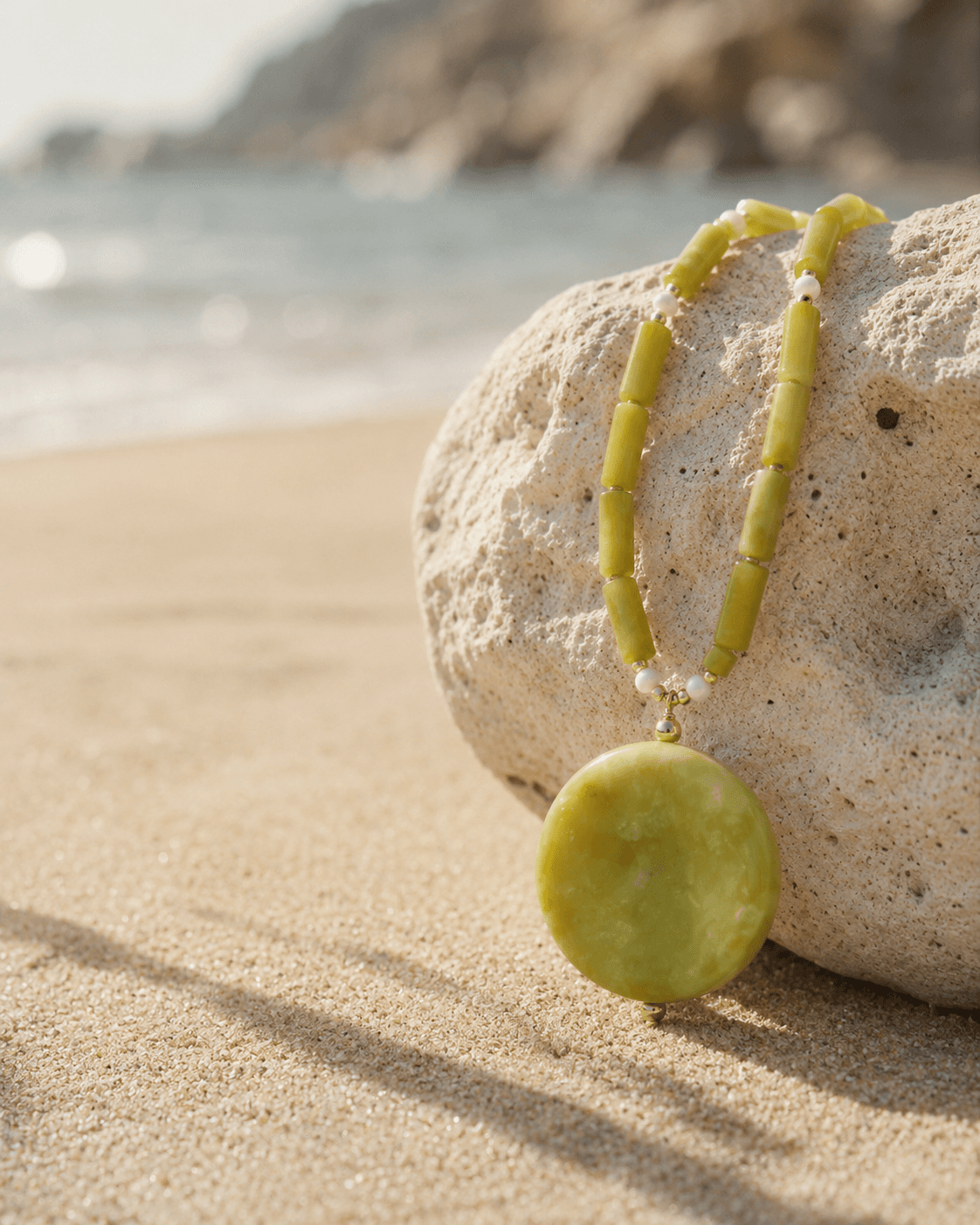 Collar de jade limón sobre una piedra clara junto al mar bajo luz de mañana.