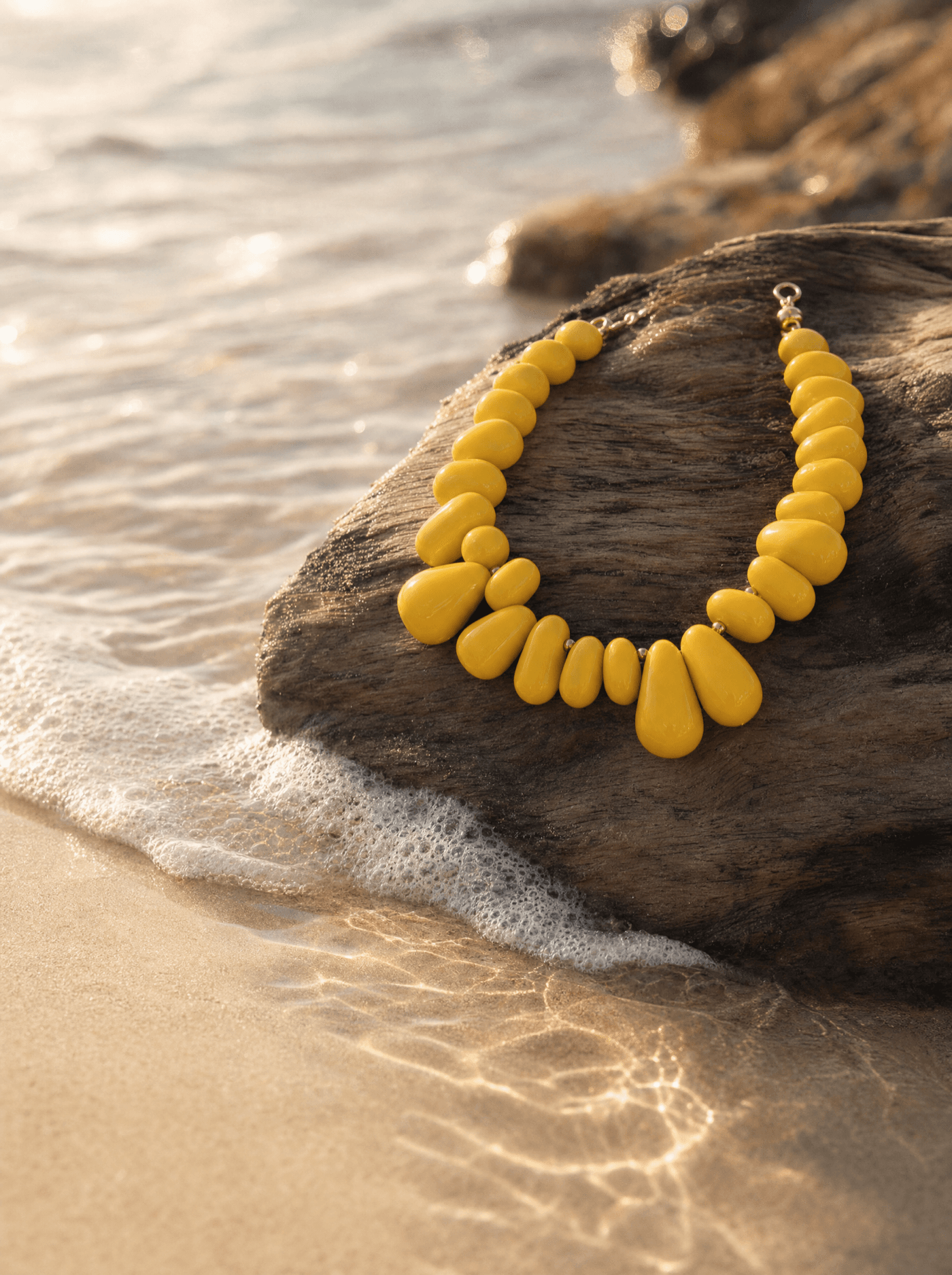 Collar de gotas amarillas sobre madera de deriva a la orilla del mar al atardecer.