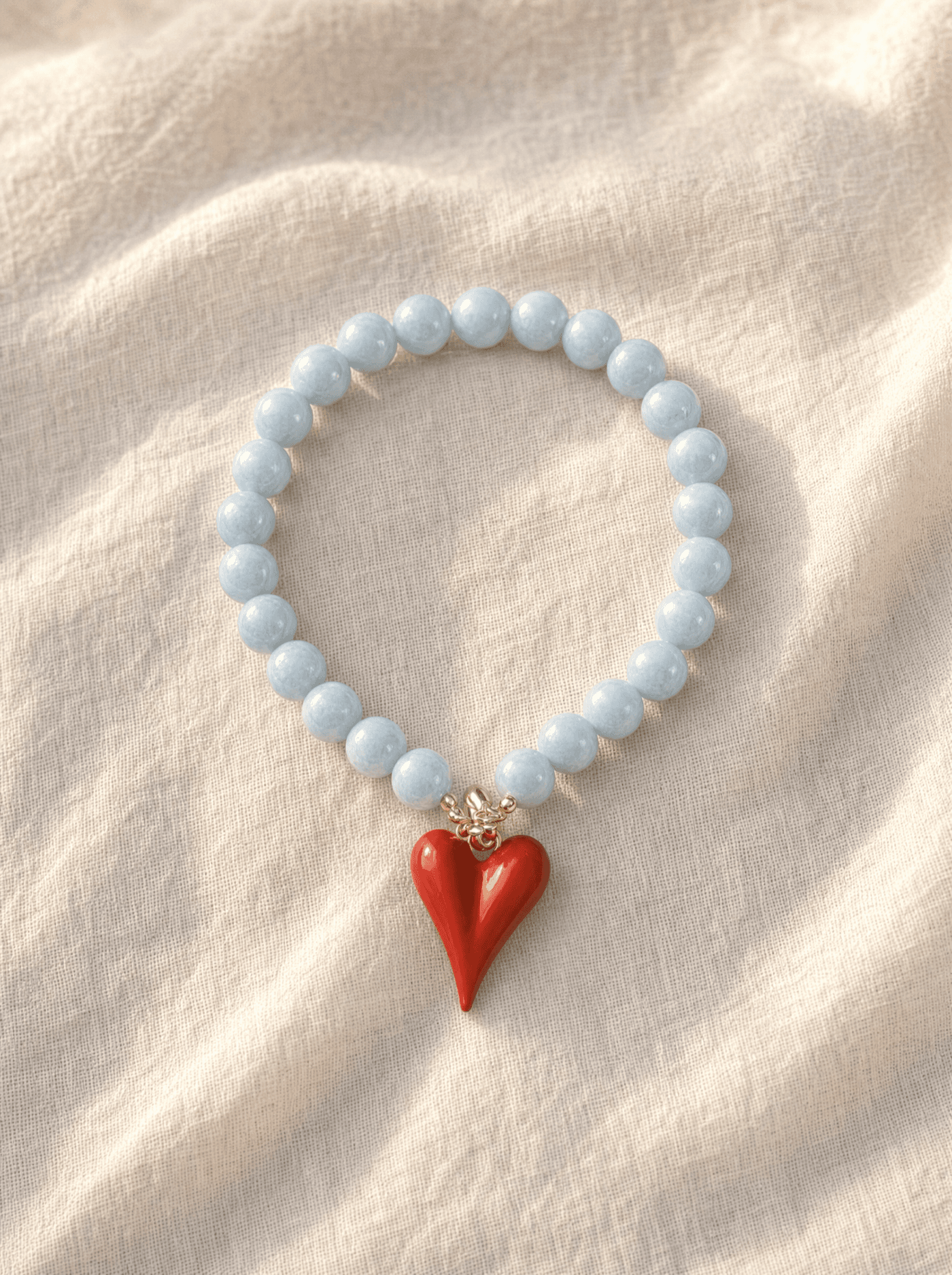 Pulsera Coral completa extendida en círculo sobre lino marfil, mostrando todas las cuentas y el corazón.