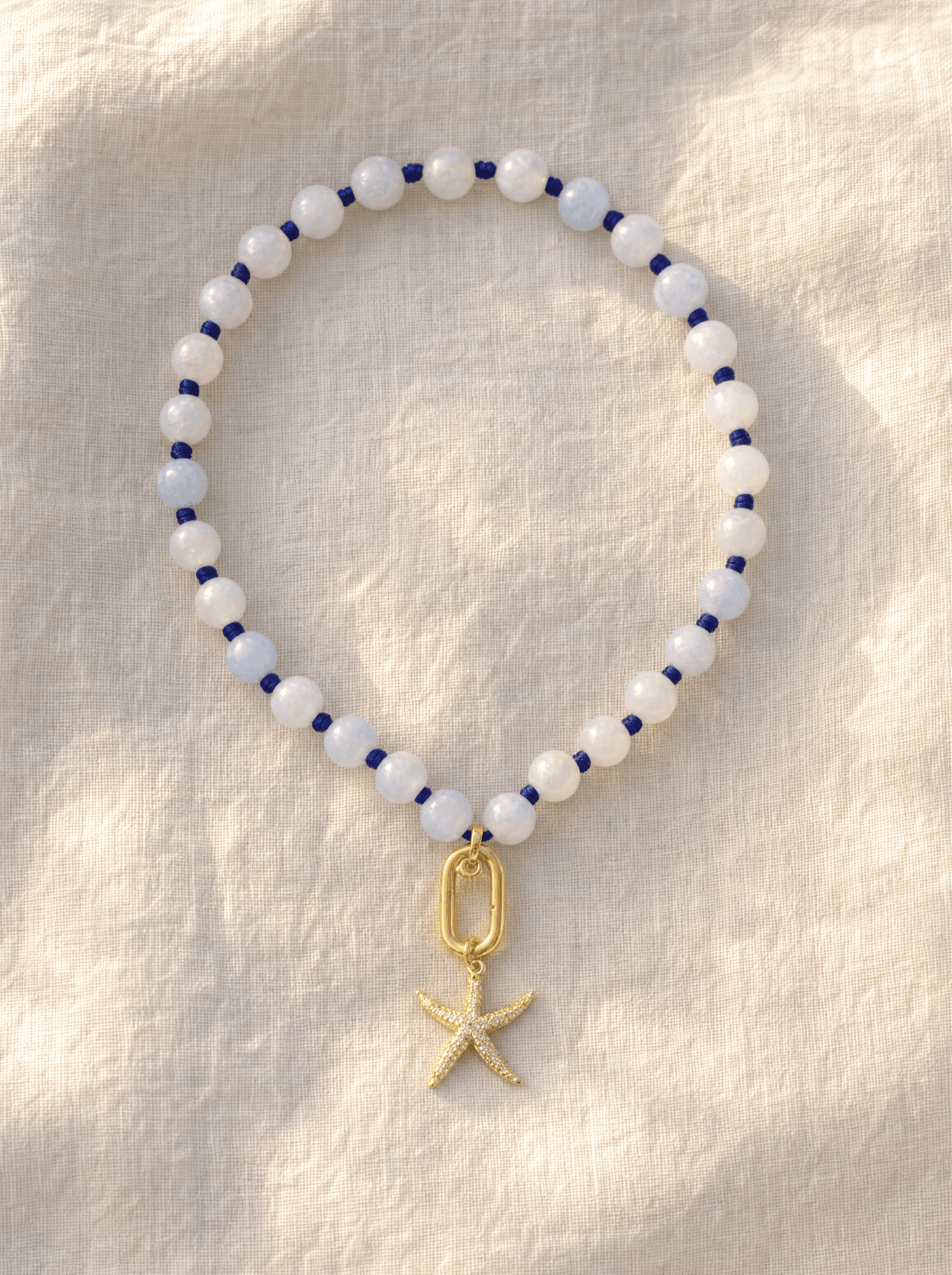 Pulsera Estrella de Mar completa extendida en círculo sobre lino marfil, mostrando cuentas, nudos y dije.